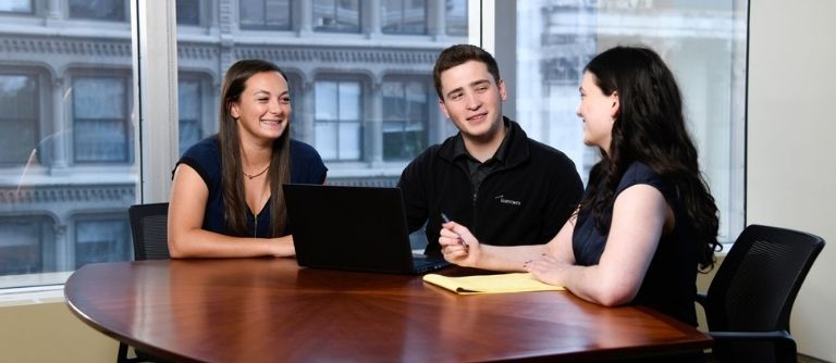 three accounting interns sitting at a table with a laptop